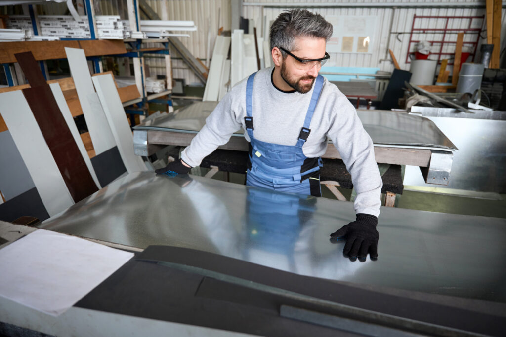 worker handling a sheet of metal in fabrication shop